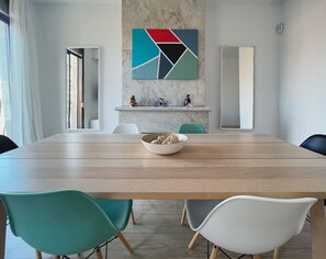 Ein moderner Besprechungsraum mit Holztisch, blau-weißen Stühlen, einer Marmorwand mit einem geometrischen Gemälde und einem kleinen Regal mit Figuren.