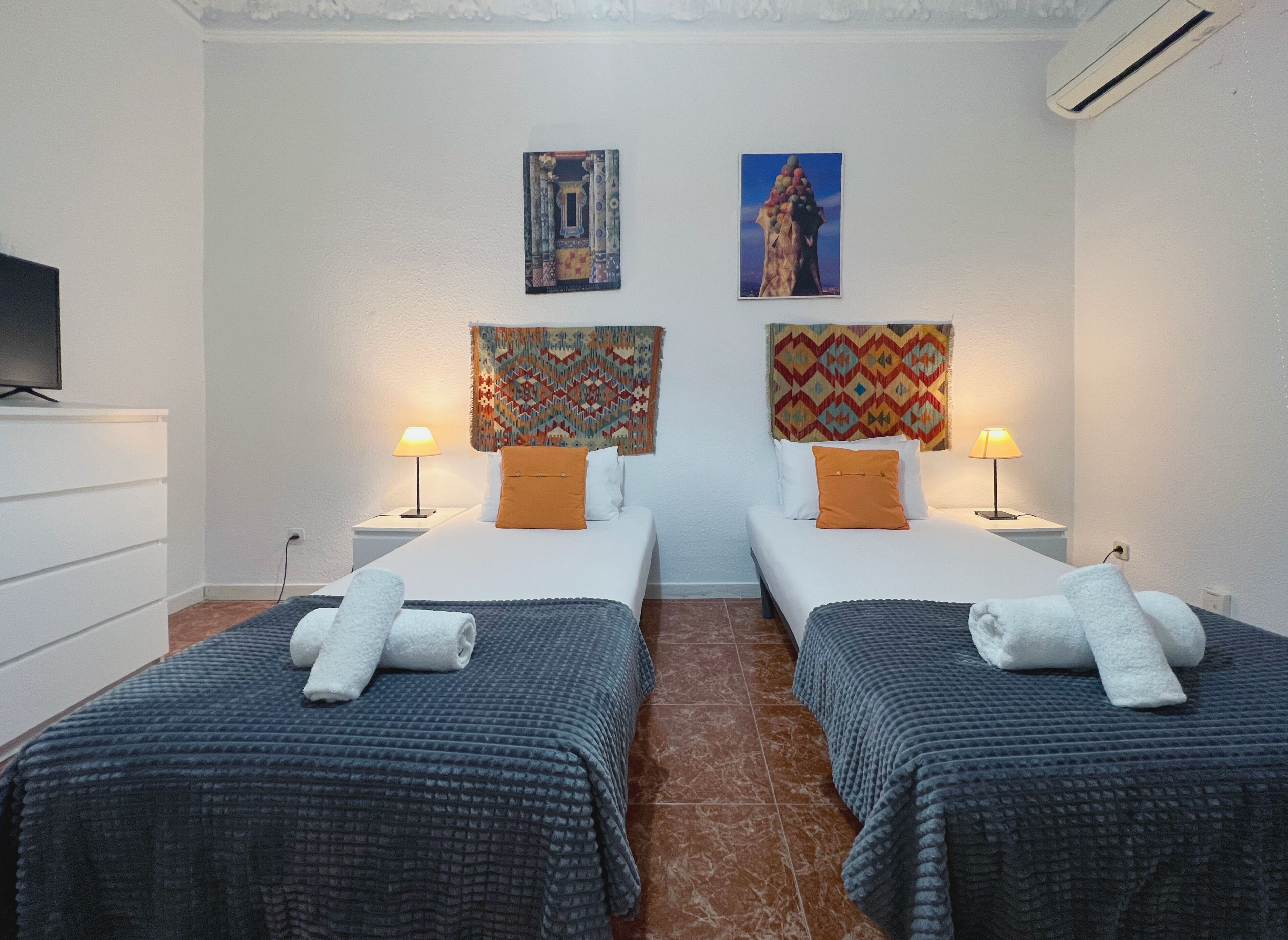 Une chambre d’hôtel avec deux lits simples, chacun doté d’une tête de lit et d’un oreiller assortis, un téléviseur à écran plat sur le côté gauche et deux lampes fixées au mur.
