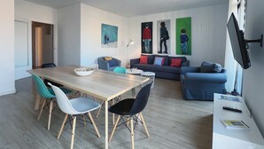 A modern living room with a dining area, featuring a wooden table, chairs, a sofa, and a TV mounted on the wall. - Stay U-nique Apartments Casanova (Barcelona)