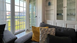Een woonkamer met een bank, kussens, een glazen kast met planken en een schuifpui naar een balkon.