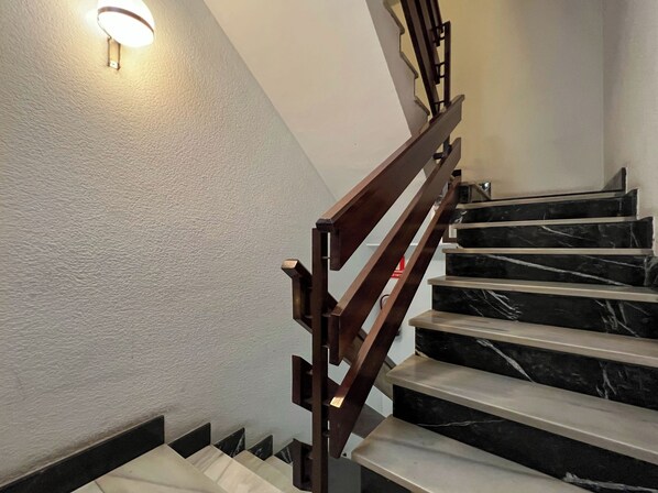 Una escalera con escalones de mármol negro y barandilla de madera, que lleva a una plataforma con una lámpara.