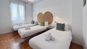 A hotel room with two beds, a large woven headboard, a small table, and a lamp.