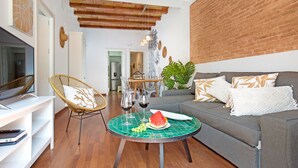 A modern living room with a grey sofa, wicker chair, and a round table with a watermelon and wine glasses. - Stay U-nique Apartments Girona (Barcelona)