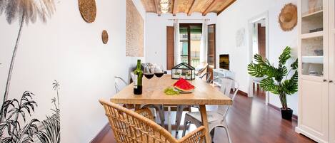Un comedor con una mesa de madera, sillas de mimbre, una planta en maceta y vistas al exterior.