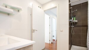 A modern bathroom with a bathtub, a shower, and a sink. There are towels on a glass shelf and a shower curtain. - Stay U-nique Apartments Girona (Barcelona)
