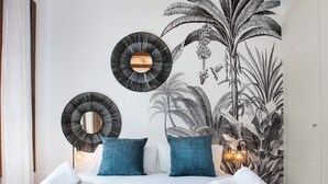 A neatly made bed with two pillows, a wall-mounted mirror, and a wall art of tropical plants. - Stay U-nique Apartments Girona (Barcelona)