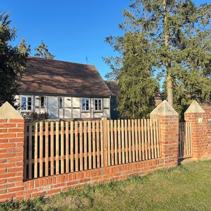 A house with a brick exterior, a wooden fence, and a clear blue sky. - Shepherd's house in the Wische, a holiday home in the nature conservation area of the Elbe (Iden)
