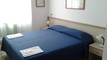 Un letto rifatto con lenzuola blu, una lampada da comodino e un piccolo tavolino con una lampada.