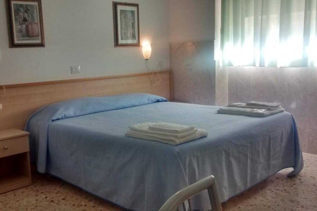 A hotel room with a single bed, a nightstand, a chair, and a window with curtains.