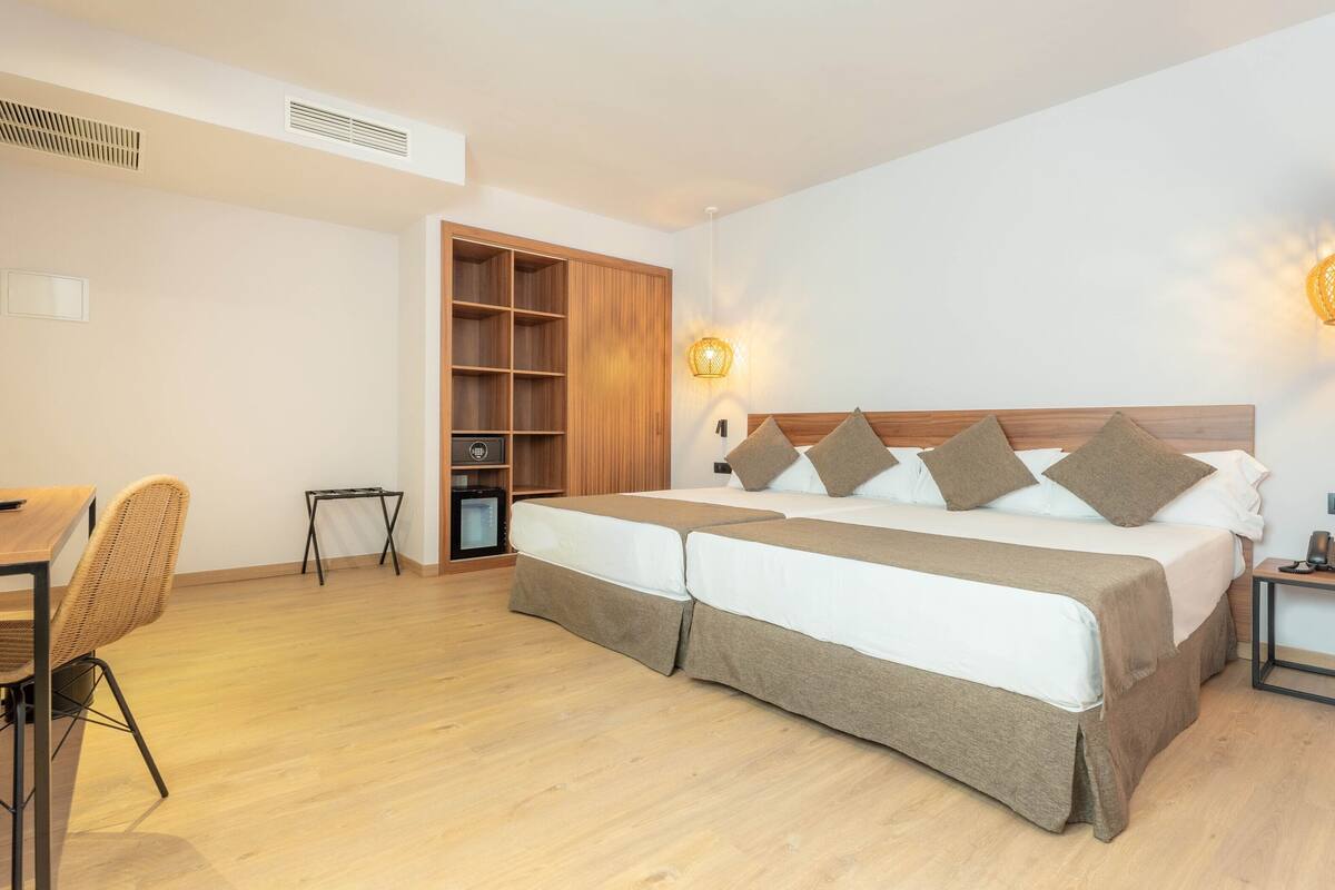 A modern hotel room with a large bed, a desk, a chair, and a wardrobe.