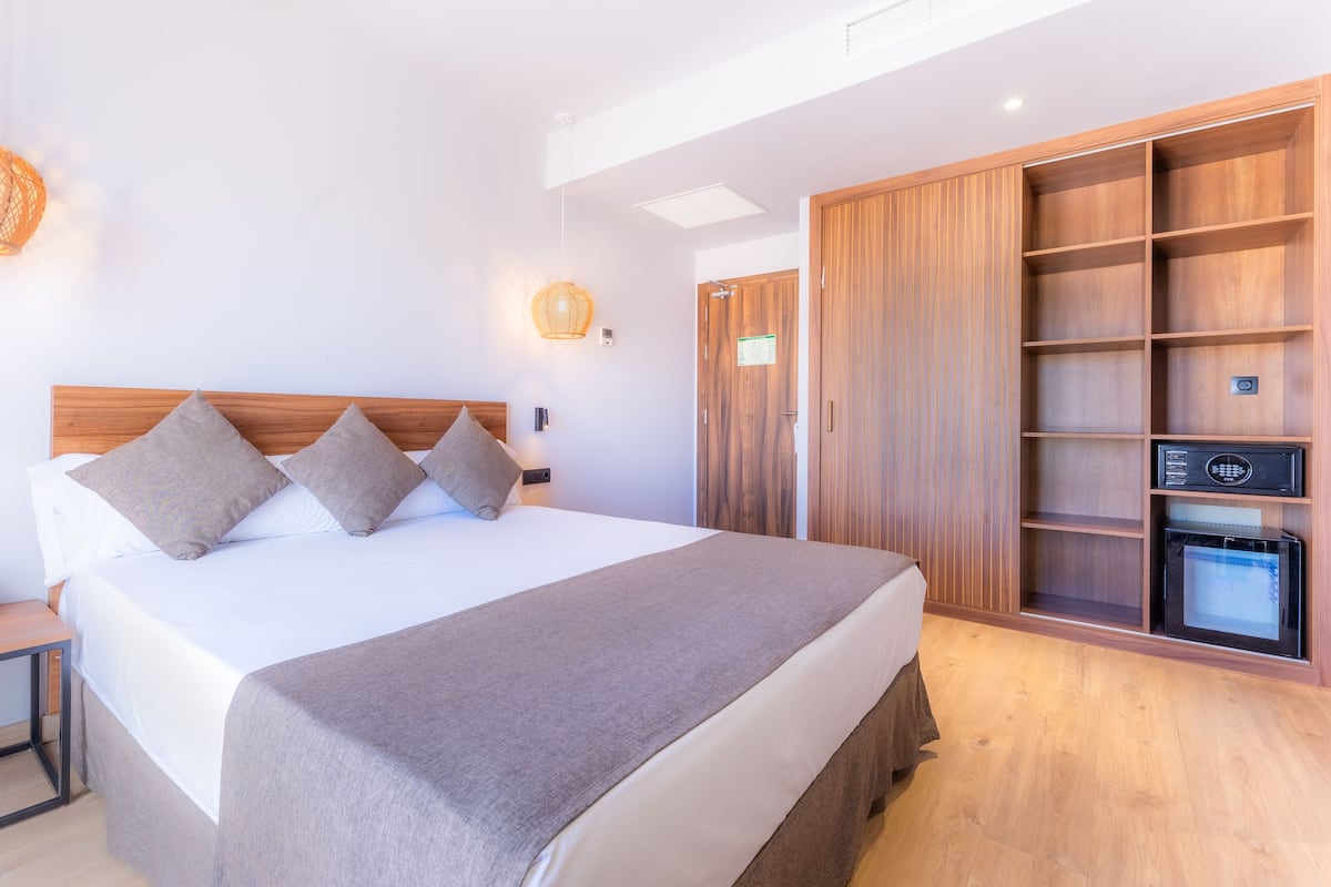 A modern hotel room with a large bed, bedside tables, a wardrobe, and a minibar.