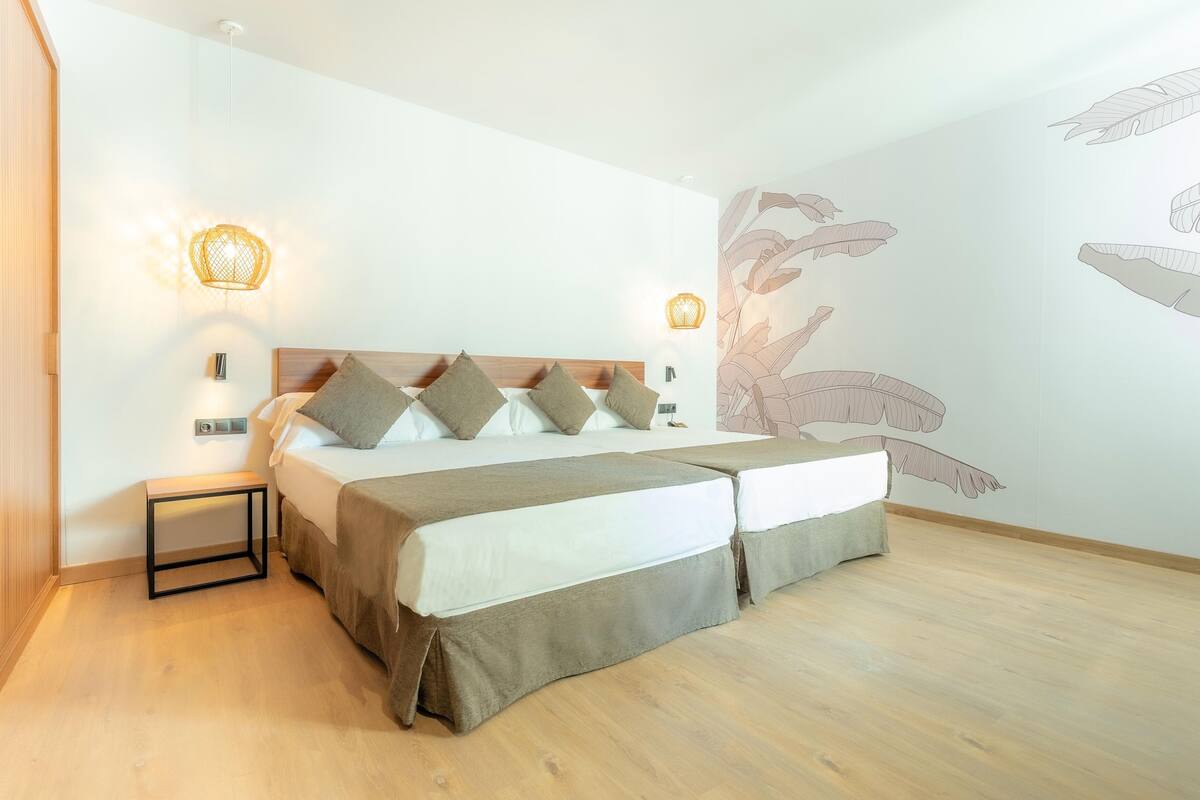 A bedroom with a wooden headboard, a bed with multiple pillows, bedside lamps, and a wall mural.