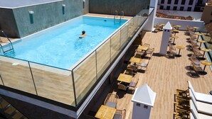 An outdoor swimming pool with a glass barrier, surrounded by wicker furniture and a tiled deck. - DWO Nopal (Puerto de la Cruz)