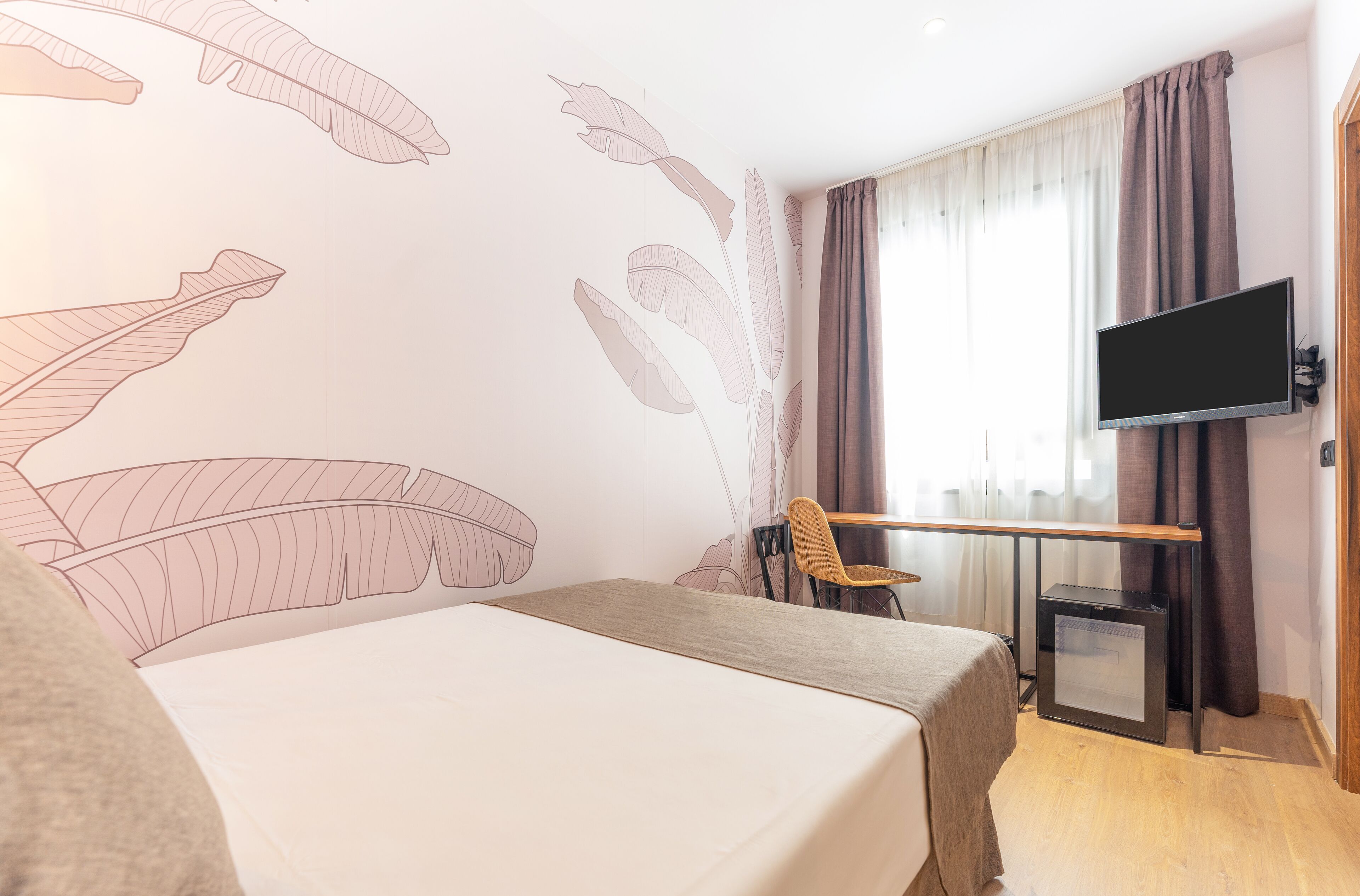 Habitación de hotel con cama, escritorio, silla, televisor y un pequeño calentador.