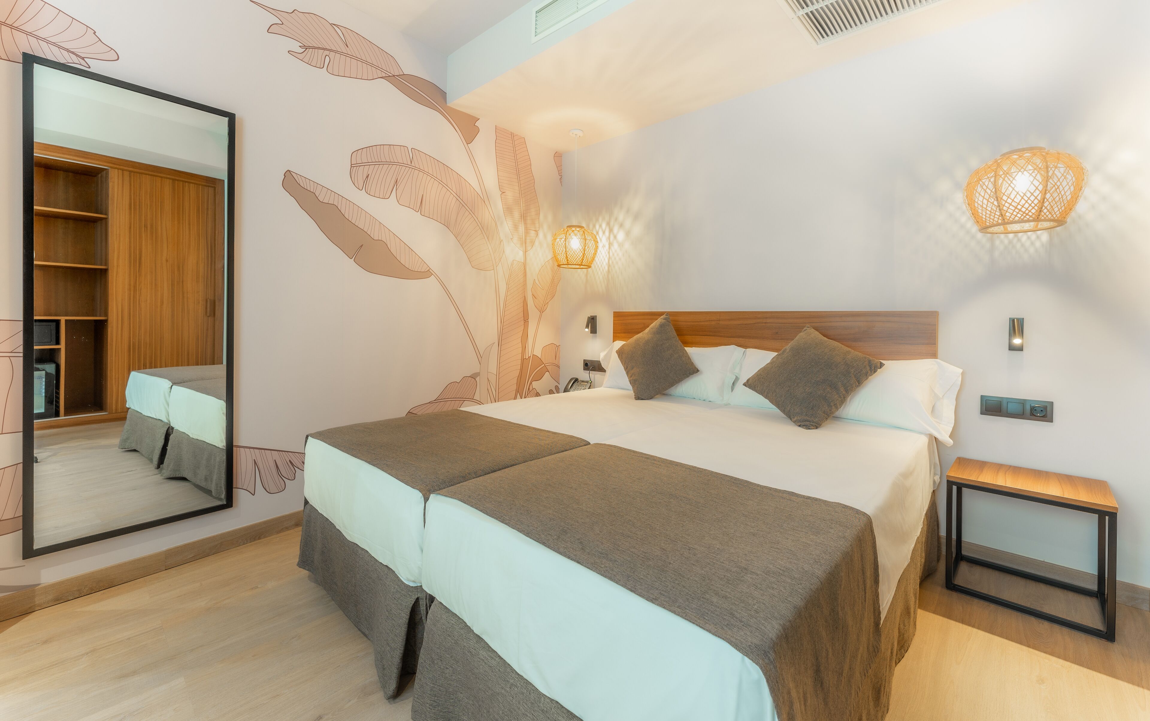 A modern hotel room with a large bed, a wardrobe, a bedside table, and a wall-mounted light fixture.
