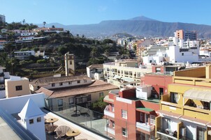 Un hotel de gran altura con múltiples balcones, una terraza en la azotea y vistas a un paisaje urbano con montañas al fondo.