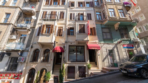 A multi-story building with a hotel on the ground floor, featuring balconies, a red awning, and a parked car. - Opera House Hotel (Istanbul)