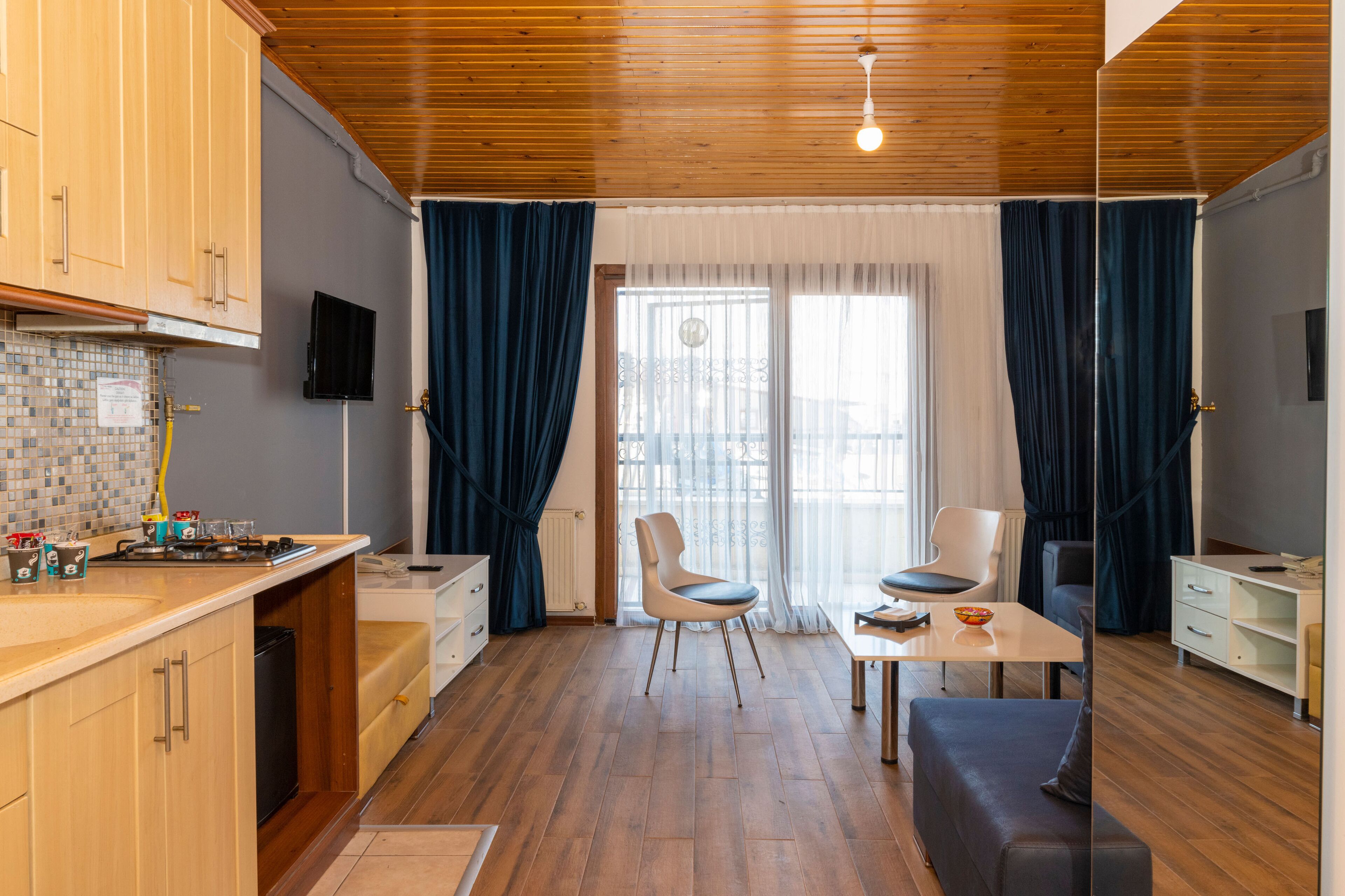 A modern kitchen with wooden cabinets, a dining area with a table and chairs, and a large window with curtains.