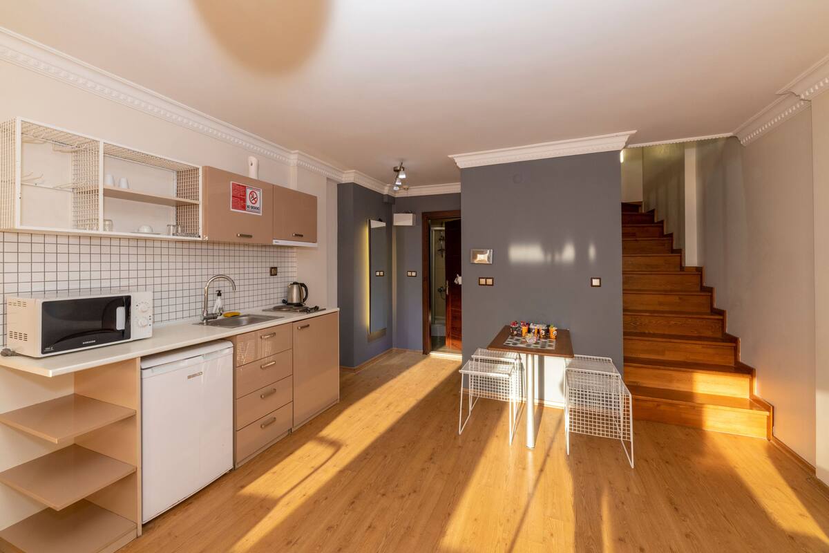 A modern kitchen with white appliances, a wooden staircase, and a dining area with a table and chairs.