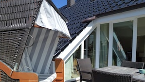 En solbeskinnet terrasse med spisebord, fletstole og markise.