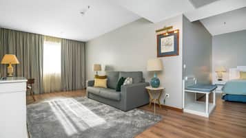 Una sala moderna con un sofá gris, dos mesitas de noche con lámparas, un estante blanco pequeño y una cama con colcha azul.