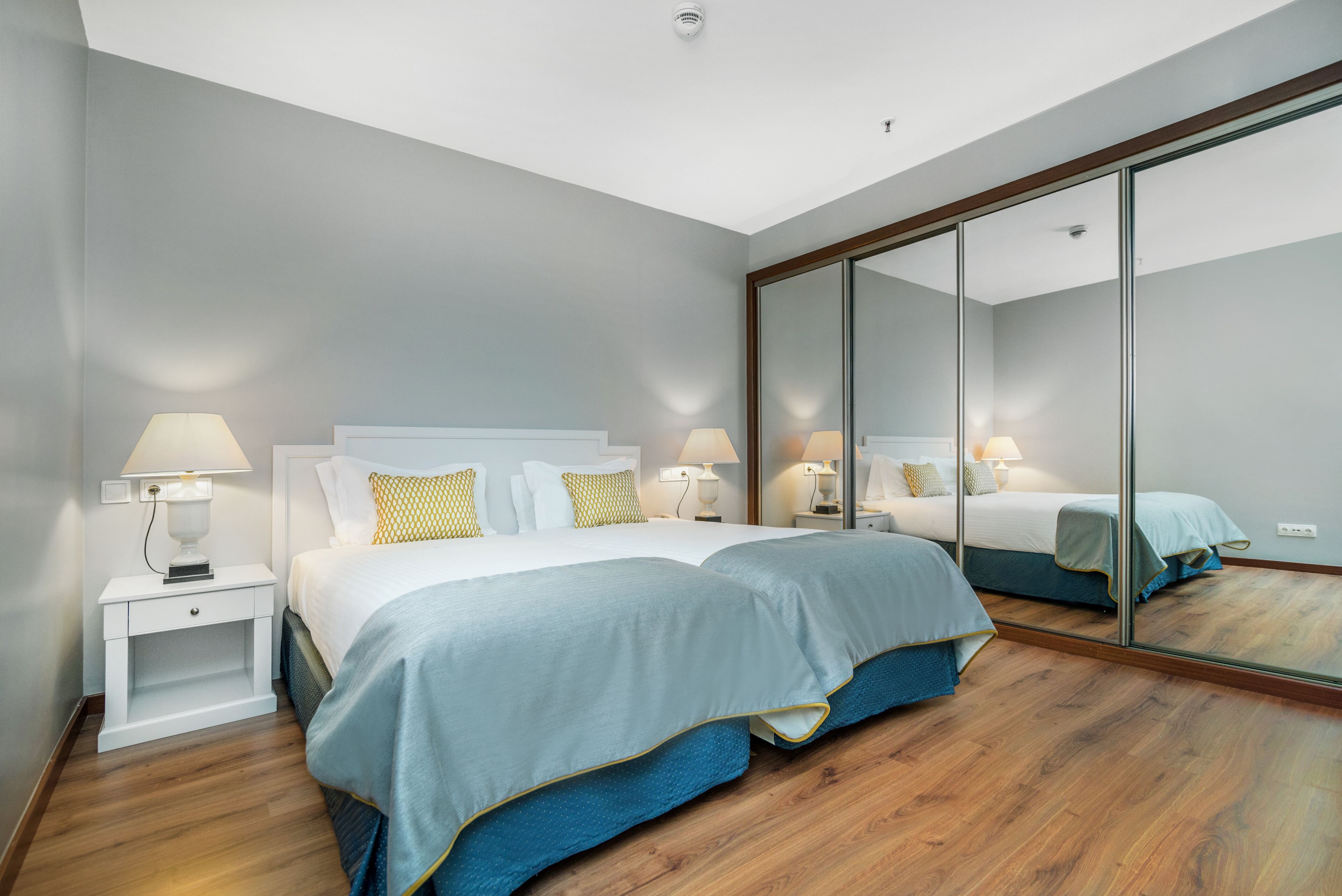 Una habitación de hotel moderna con una cama grande, mesitas de noche con lámparas y un espejo amplio.