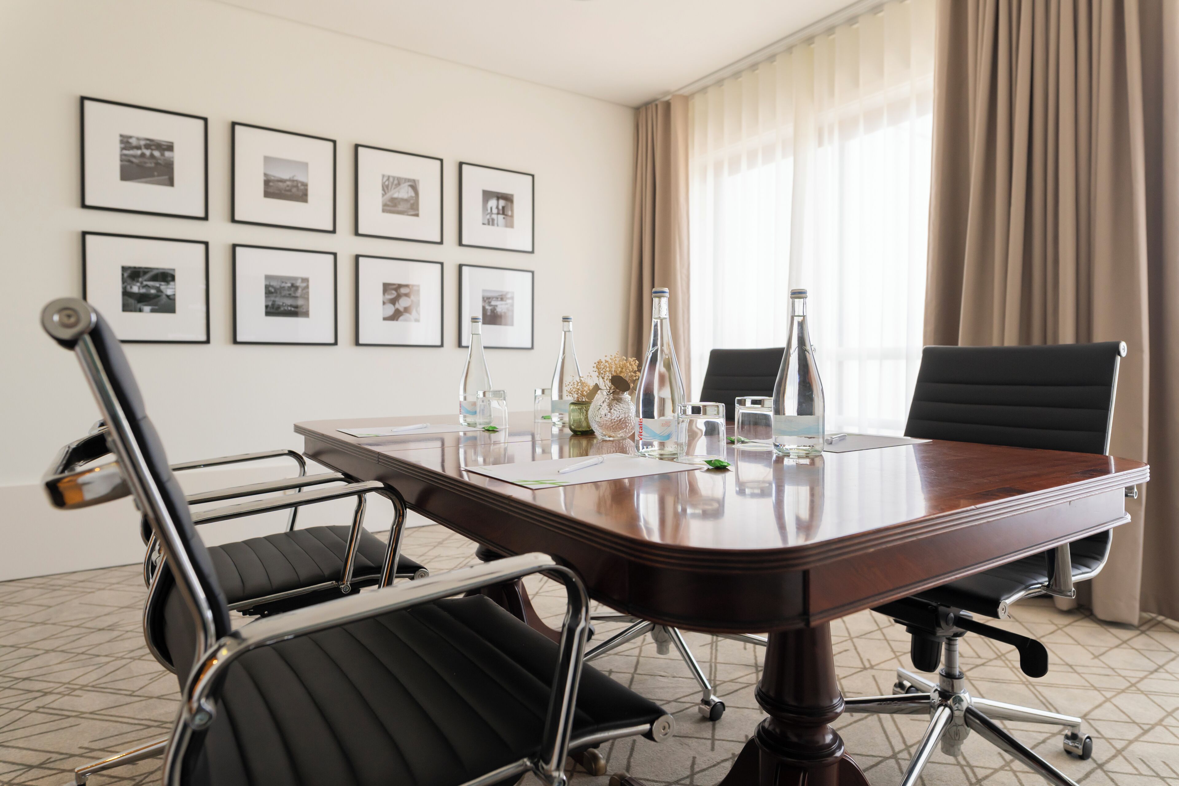 A conference room with a large table, two black office chairs, and framed pictures on the wall.