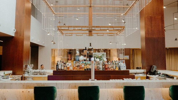 A modern bar area with a high ceiling and glass panels, wooden accents, and green bar stools. - Gaia Residence (Vila Nova de Gaia)