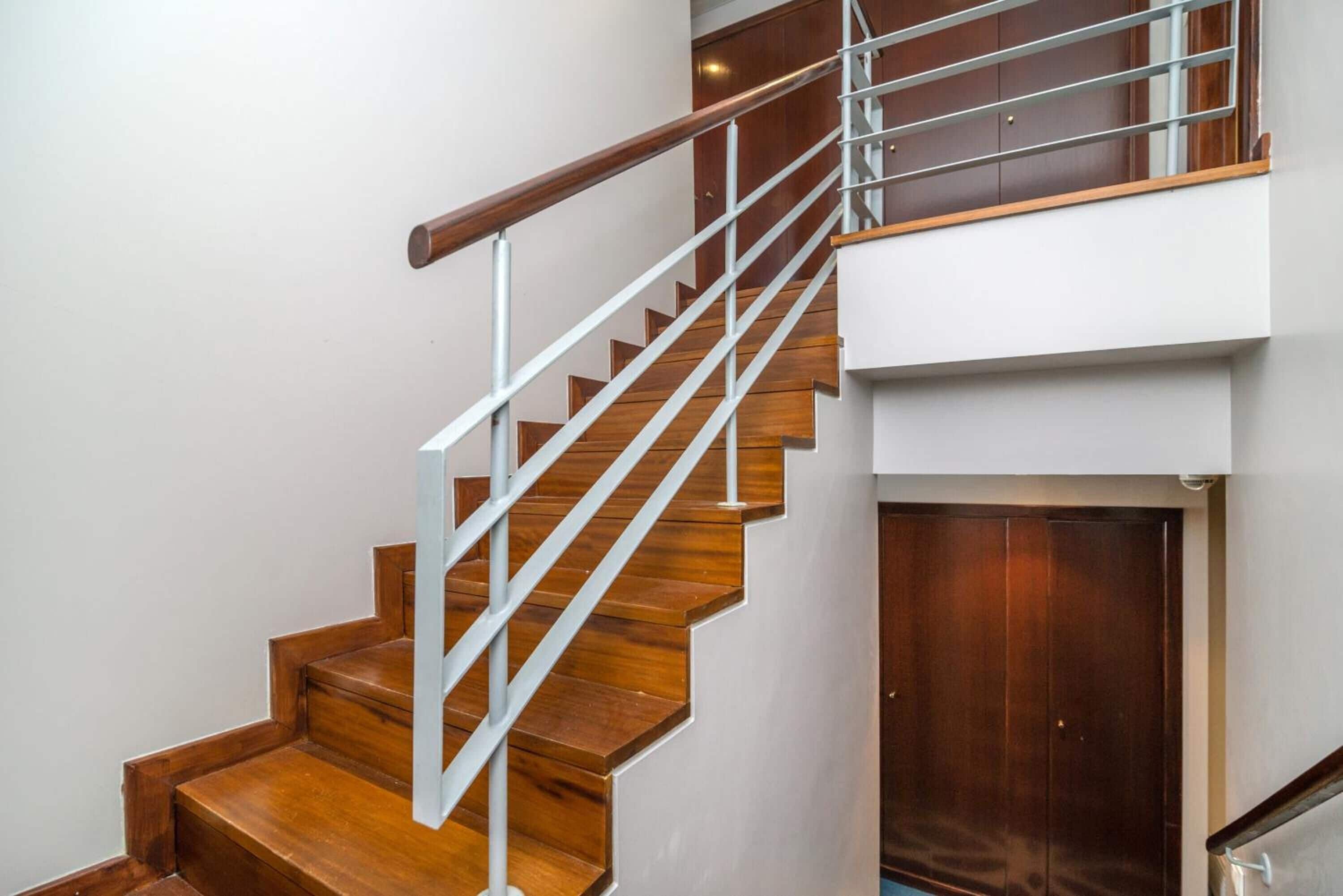 A staircase with wooden steps and a metal handrail, leading to a landing with a door.
