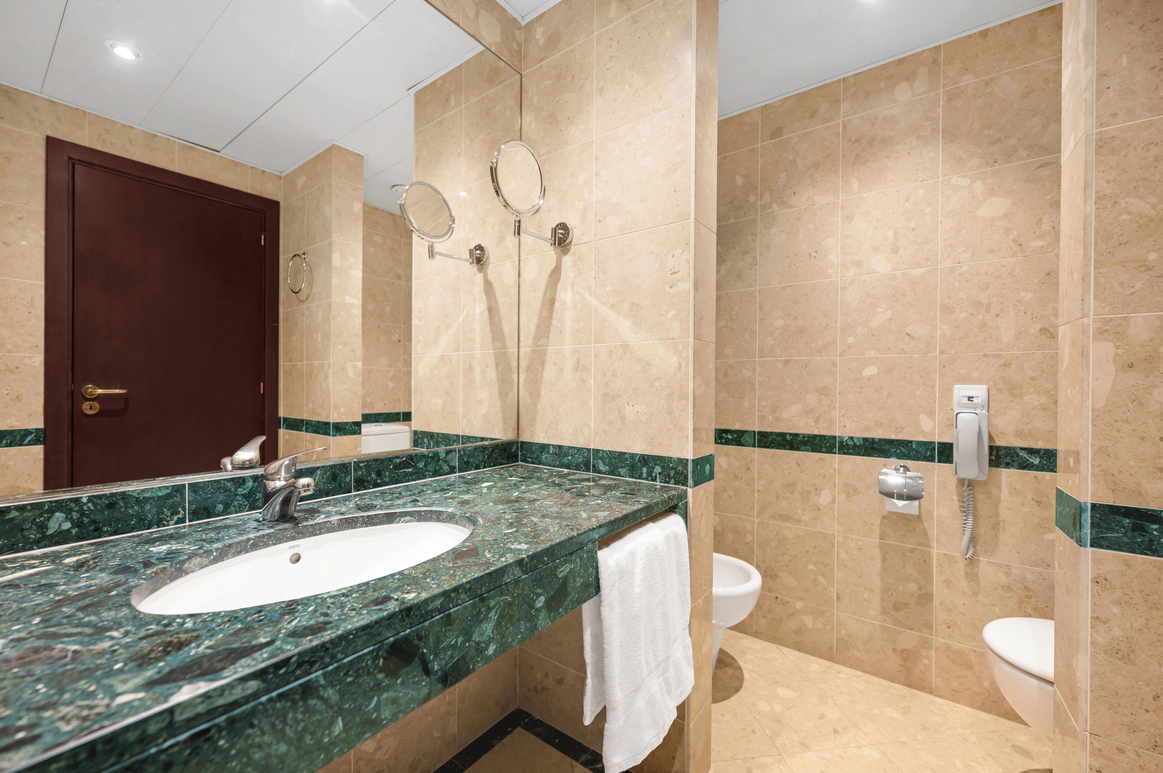 Une salle de bain avec un lavabo en marbre, deux miroirs, des toilettes et une porte.