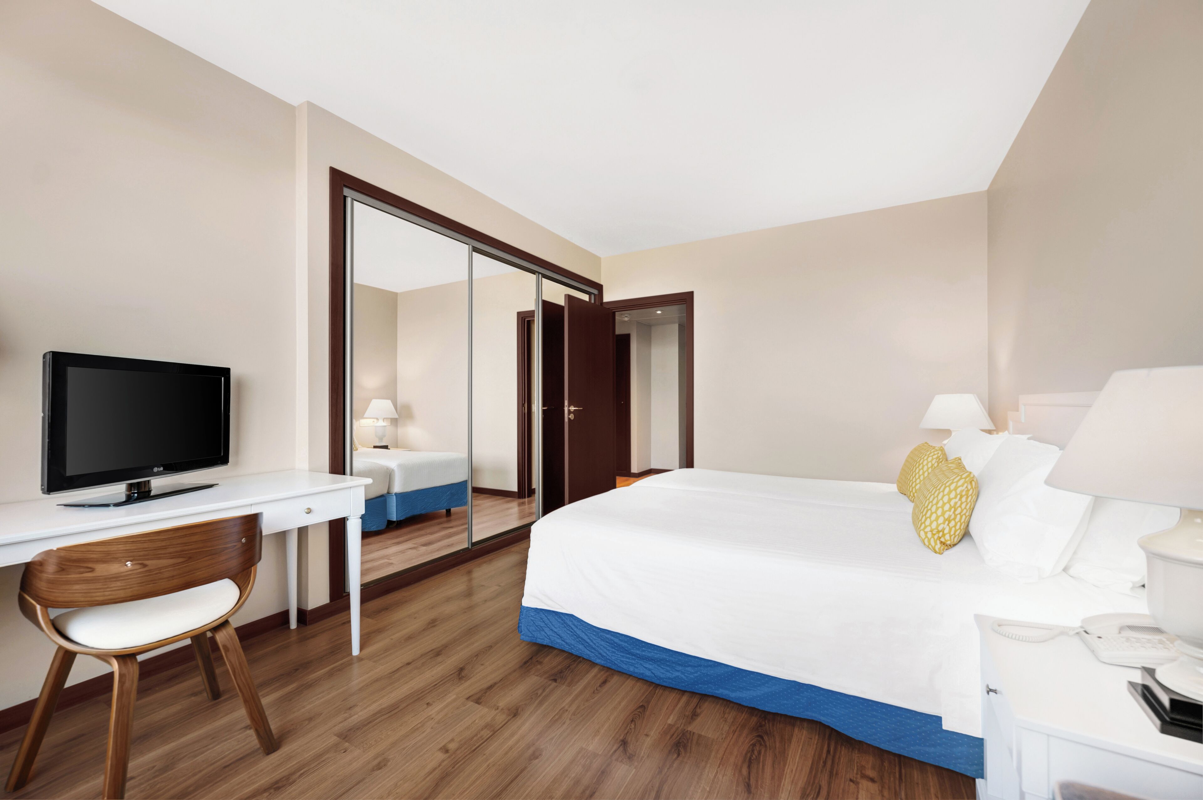 Habitación de hotel con cama, escritorio con televisor, silla, mesita de noche con lámpara y armario.
