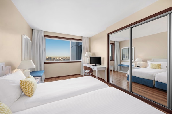 A hotel room with a large bed, a desk with a computer, a TV, and a view of the city. - Gaia Residence (Vila Nova de Gaia)