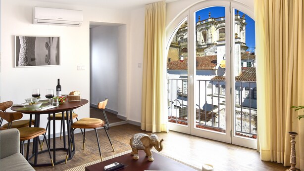 A modern living room with a dining area, a large window with a view of historic buildings, and a small elephant figurine on the floor.
