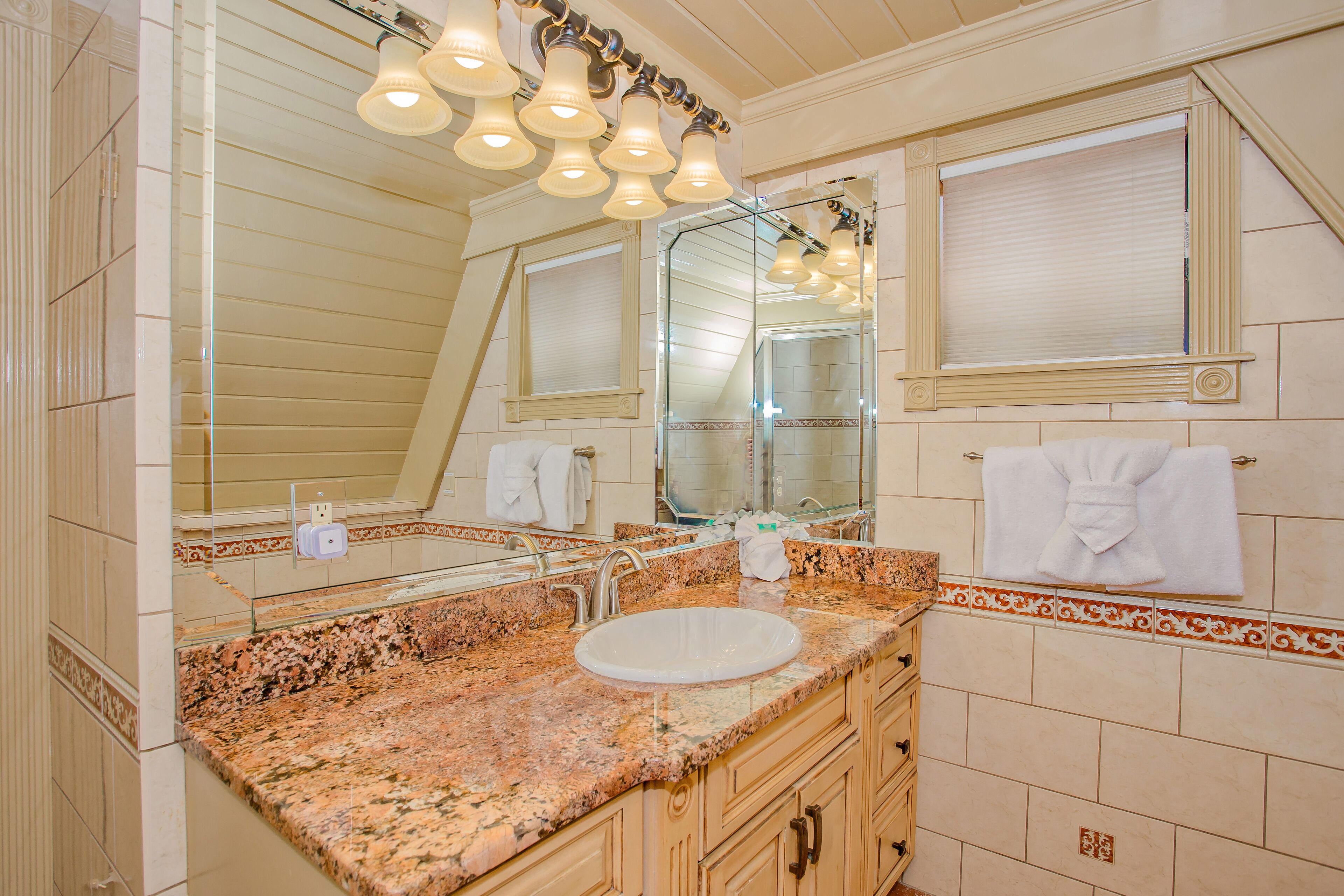Ein Badezimmer mit einer Granitplatte, einem weißen Waschbecken, einem großen Spiegel und einem Handtuch an der Wand.