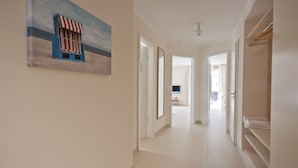 A hallway with a beach-themed painting, a ceiling light, and a view into a room with a TV and a bed. - Baltic Sea Lodges, Deck 1, elevator, wellness area, close to the beach, family friendly (Niendorf)