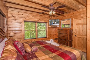 Une chambre située dans un chalet en rondins, avec un lit, un ventilateur de plafond, une télévision et une commode en bois.