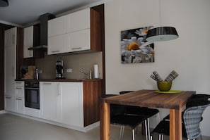 A modern kitchen with white and wooden cabinets, a built-in oven, and a dining area with a wooden table and black chairs. - Baltic Sea lodges, deck 2 with terrace, elevator and wellness area, near the beach (Niendorf)