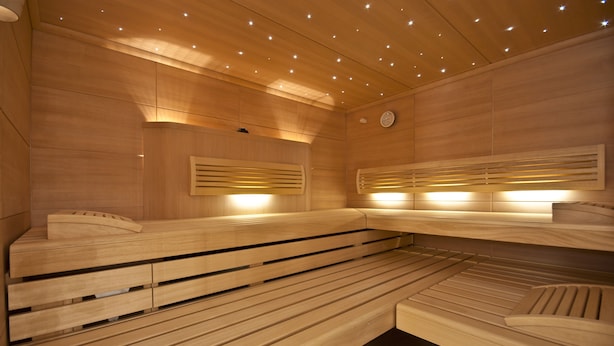 Un sauna avec des bancs en bois et des parois à lattes, équipé d’un éclairage au plafond.