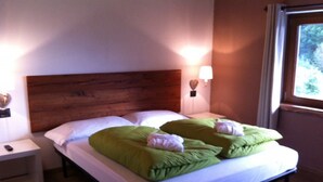 A neatly made bed with green pillows and a wooden headboard in a room with a nightstand and a wall-mounted lamp. - B&B Il Mortirolo (Mazzo di Valtellina)