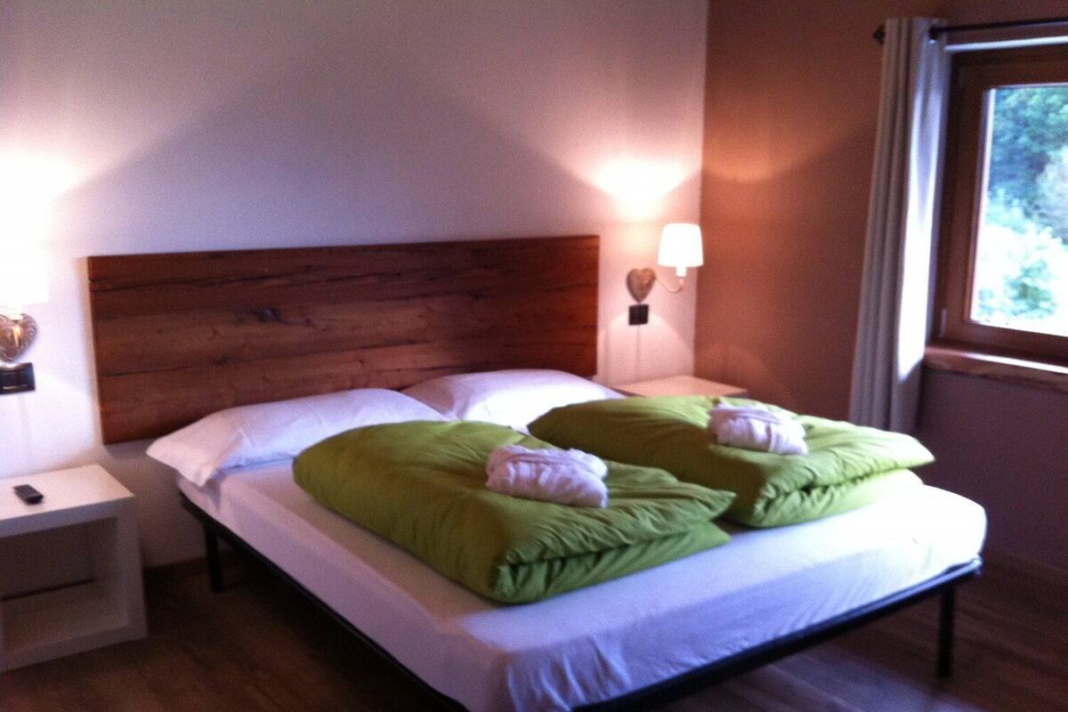 A neatly made bed with green pillows and a wooden headboard in a room with a nightstand and a wall-mounted lamp.