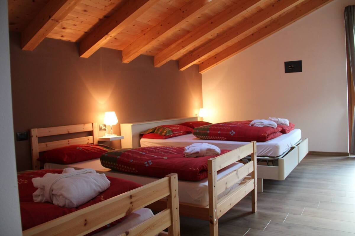A room with two wooden beds, each with red bedding and pillows, and a white mattress on the floor. There are two bedside tables with lamps.