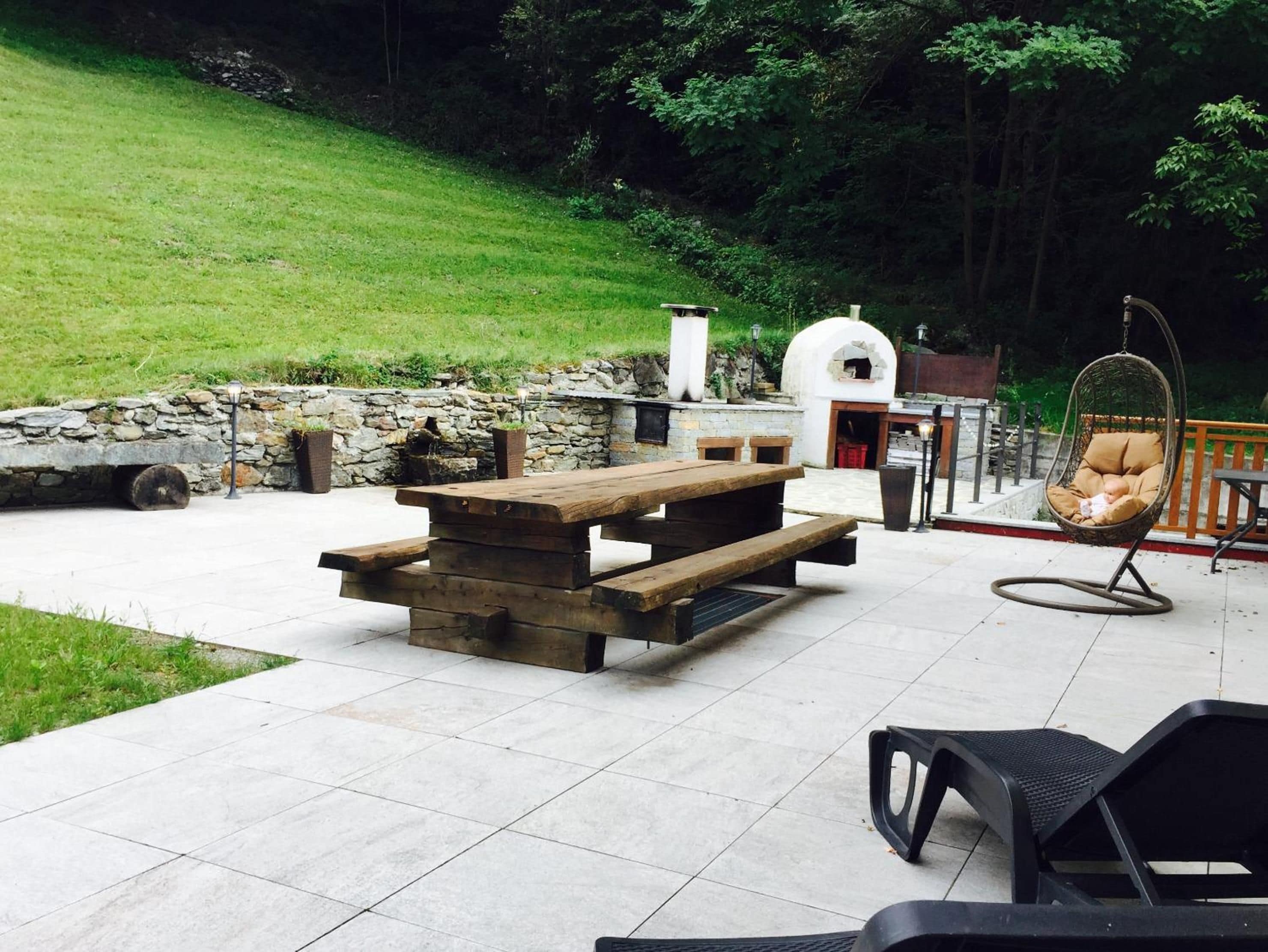 Una veranda esterna con tavolo da picnic in legno, una sedia a dondolo e un muro in pietra.