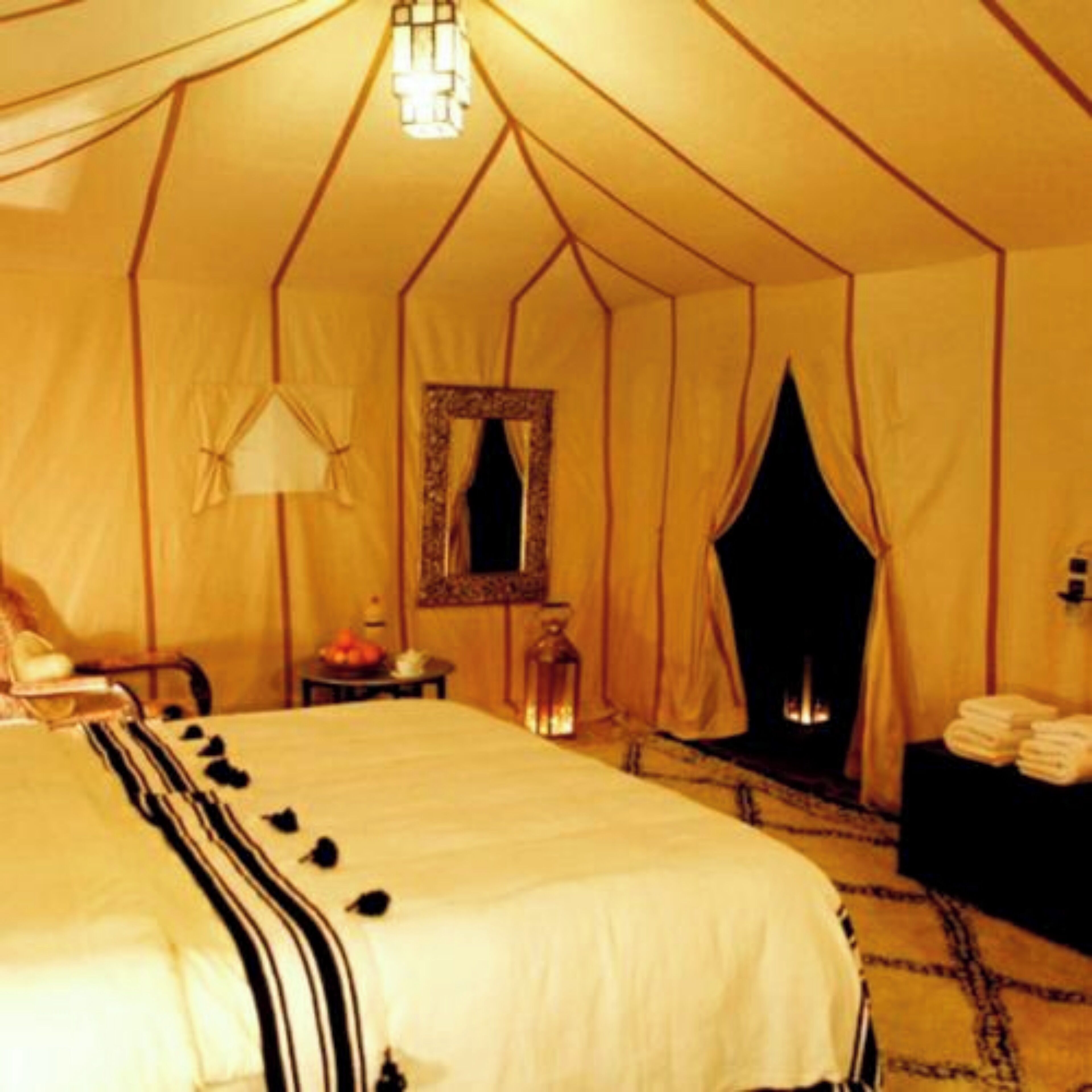 A tented room with a bed, a mirror, a table with a lamp, and a fireplace.