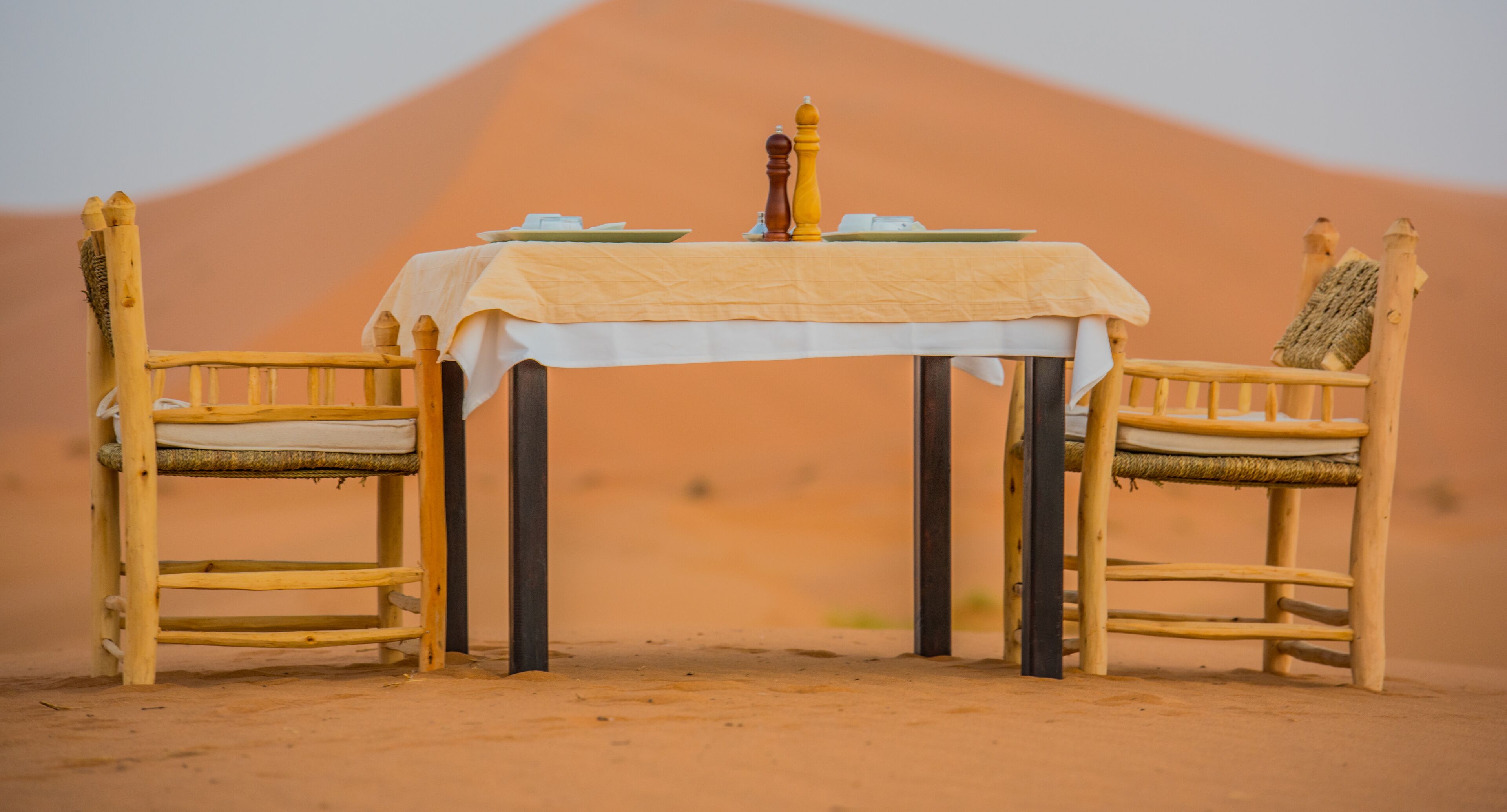 Una mesa de comedor con mantel blanco, dos sillas de madera y un salero.