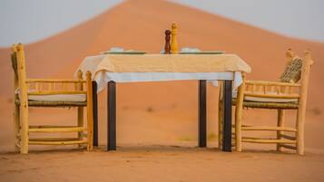 Una mesa de comedor con mantel blanco, dos sillas de madera y un salero.