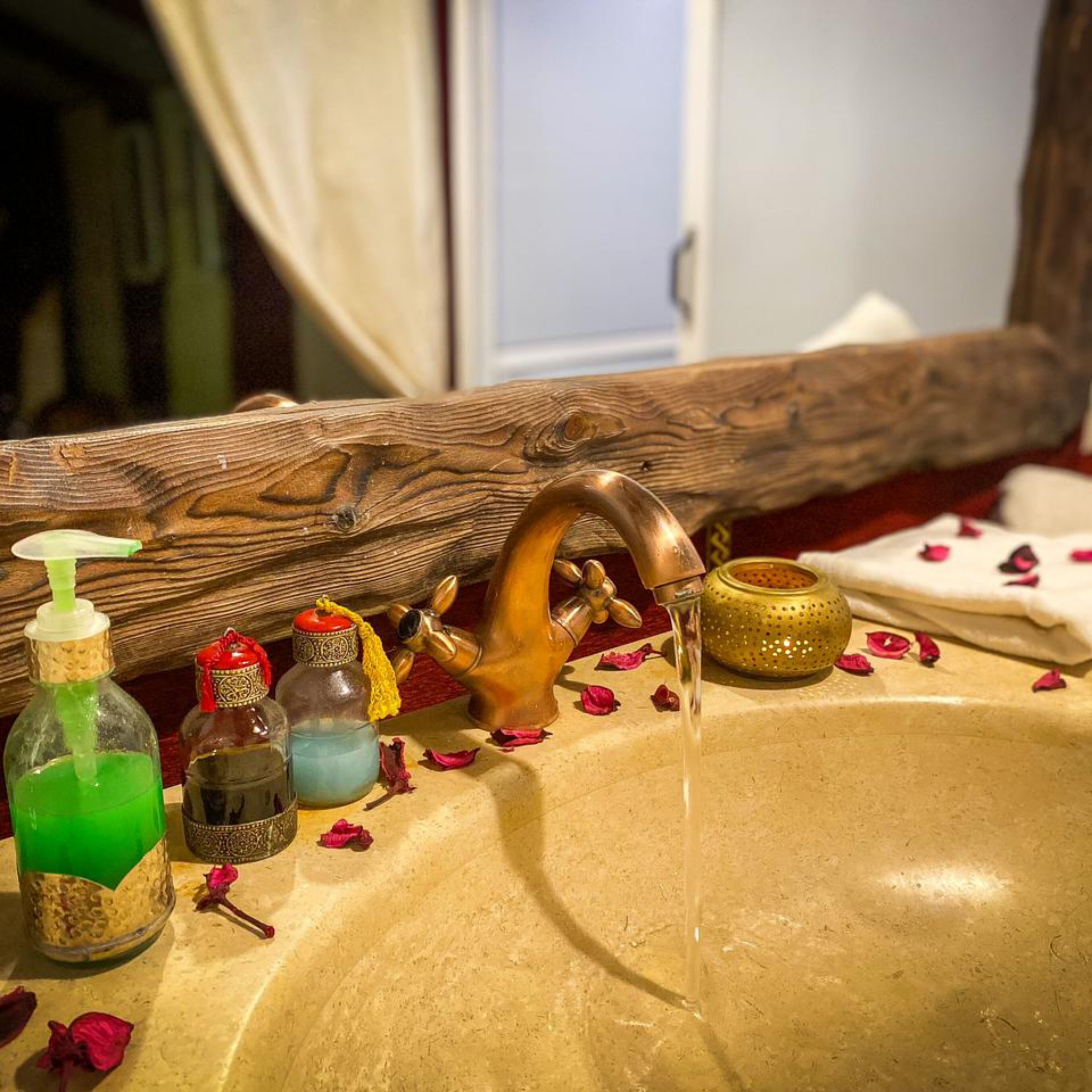 Un lavamanos de baño con grifo de madera, dispensador de jabón y varias botellas de líquidos.