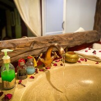 Un lavamanos de baño con grifo de madera, dispensador de jabón y varias botellas de líquidos.
