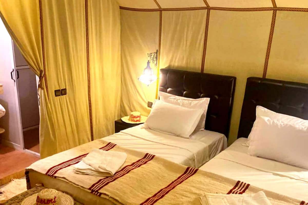 A double bed with white and red striped bedding, a bedside table with a hat, and a small table with a hat.