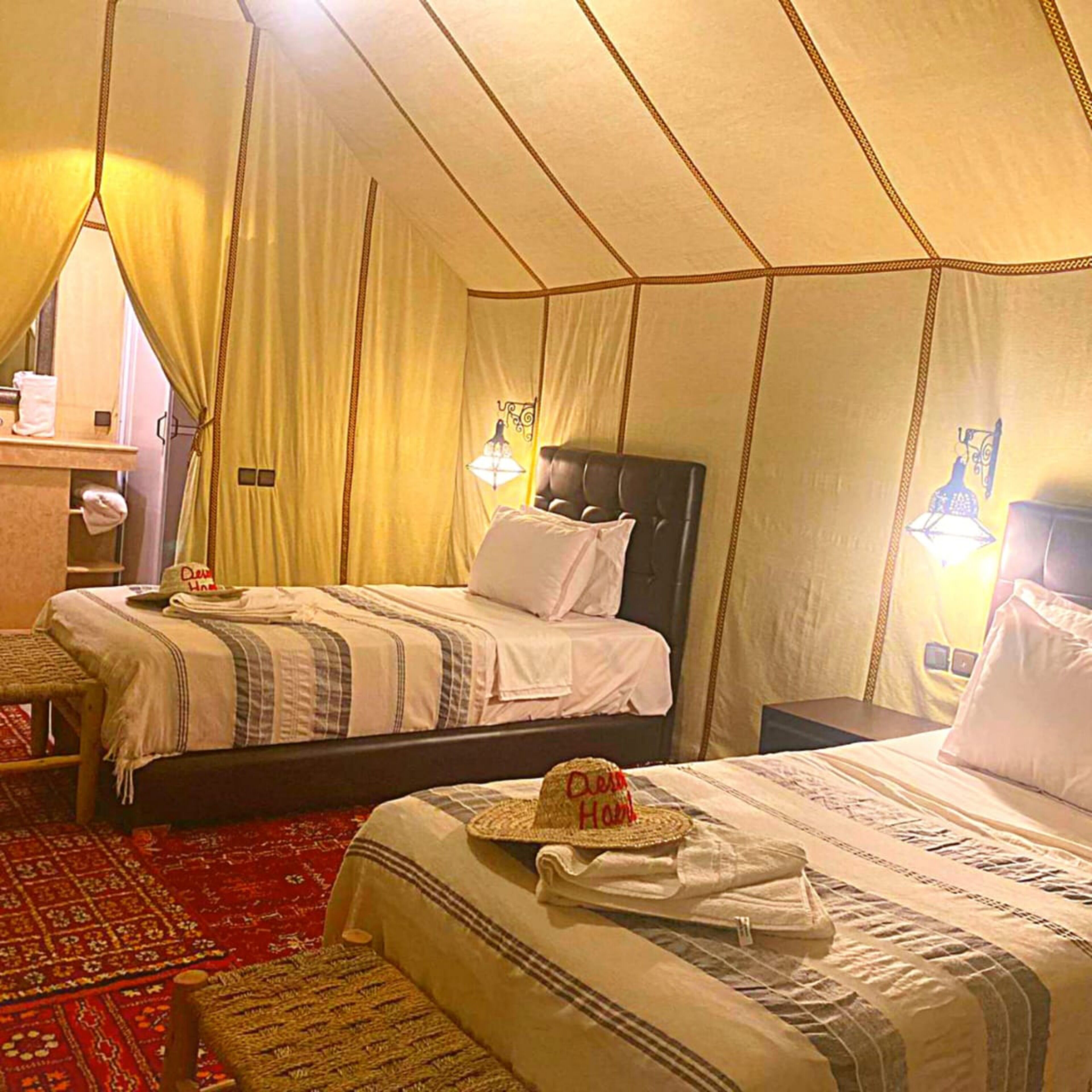 A tent-style room with two beds, a small table, and a chair.