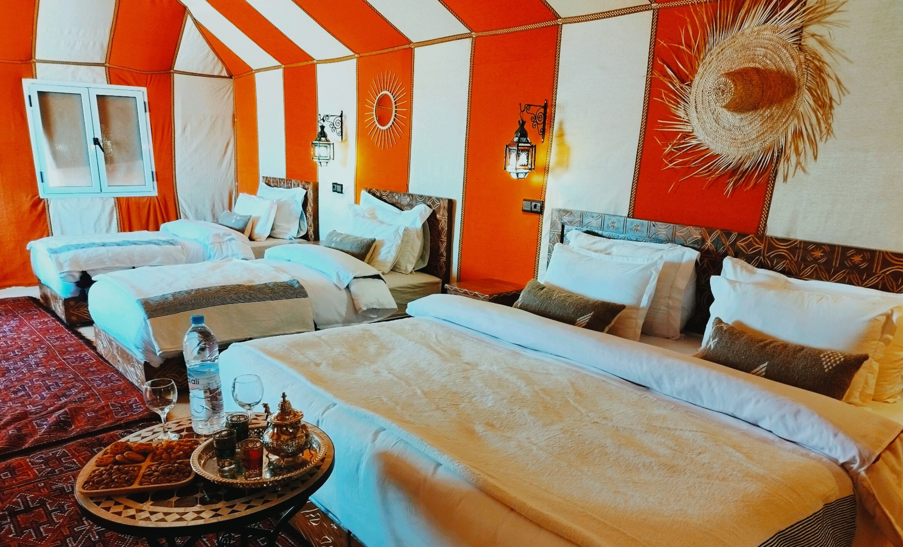A hotel room with three beds, a large sun decoration on the wall, and a traditional tray with snacks and drinks.